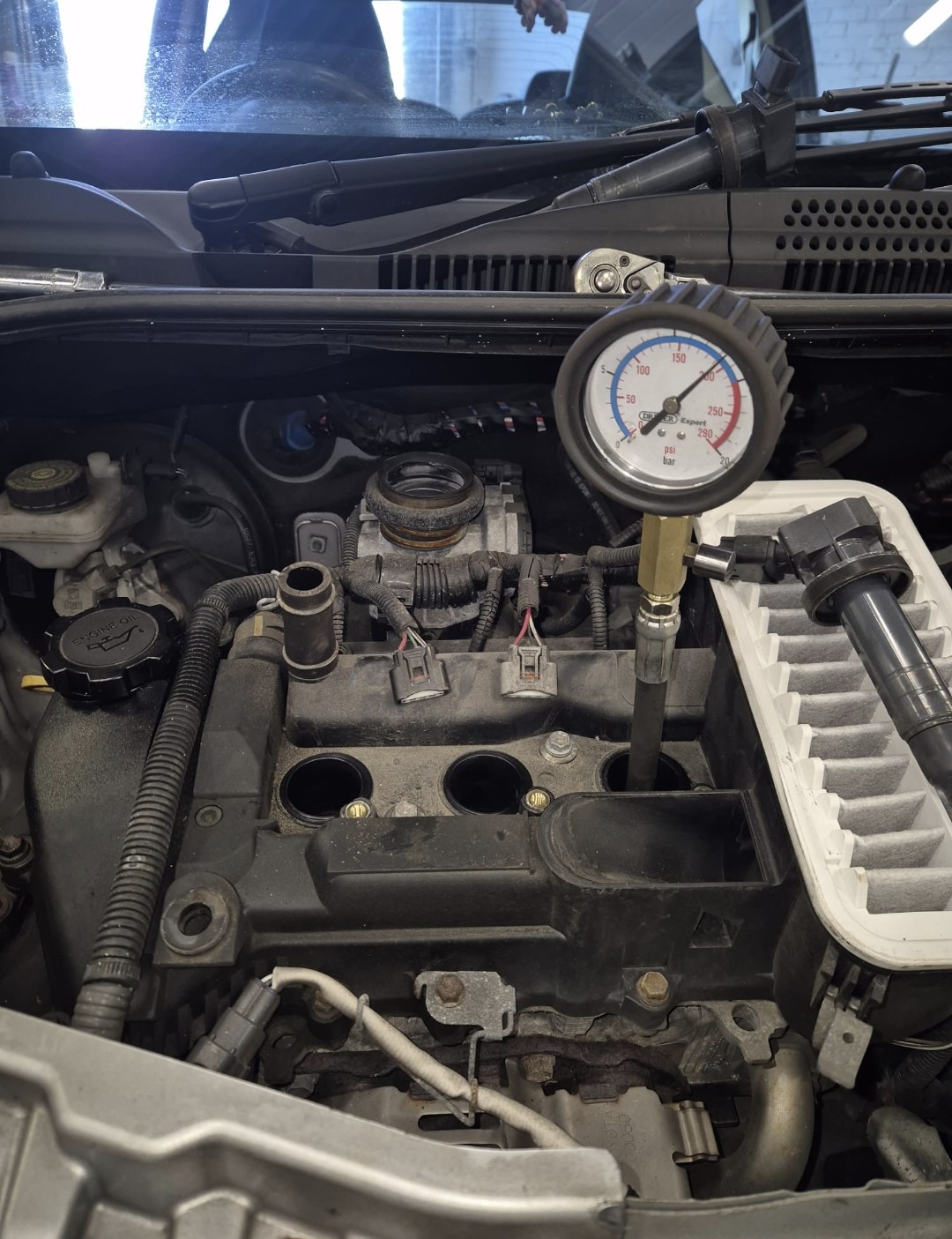 A compression test gauge screwed into a spark plug hole in an engine bay
